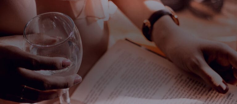 Person reading a book and holding a glass of white wine
