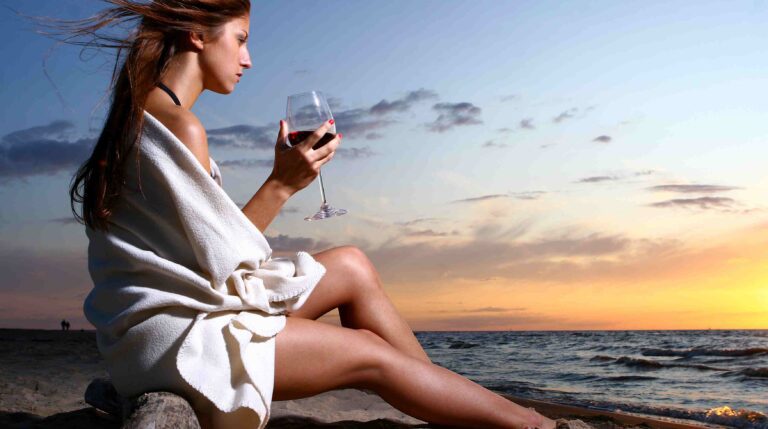 a beautyful young woman drinking wine on the beach
